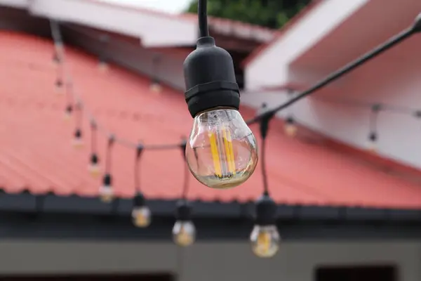 Close up view of a small globe shaped Edison style LED bulb which has orange color filaments and clear amber glass. This outdoor decoration string bulb is attached in a row. Daytime view
