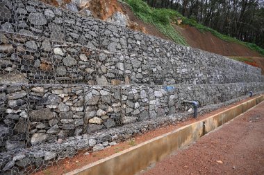 Sri Lanka 'daki bir dağ yolunda toprak kaymalarını önlemek için granit kayalarla örülmüş altıgen tel örgülerden oluşan yeni inşa edilmiş gabion duvarların (bariyer duvarlar) görüntüsü.