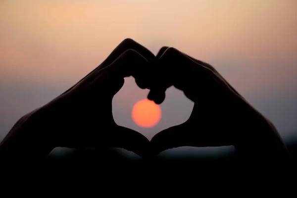 heart shaped human hand silhouette sunset background