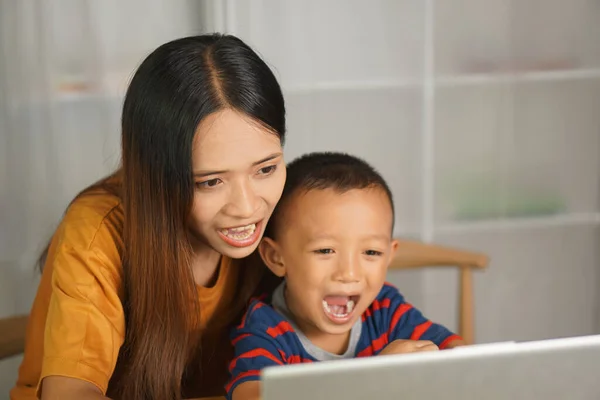 mother and son watching movies on computer at home table