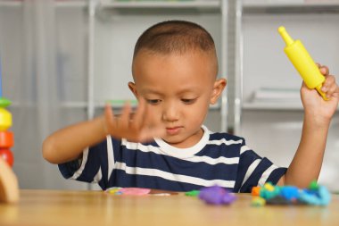 Çocuk, evdeki masada gelişimi teşvik etmek için plasticin yapıyor. Plastikler çocukları mutlu etmek ve eğlendirmek için birçok renge bürünür..