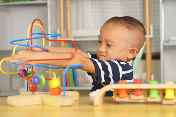 Мальчик играет с развивающими игрушками на столе в доме. Путем скольжения мяча по изогнутой стали