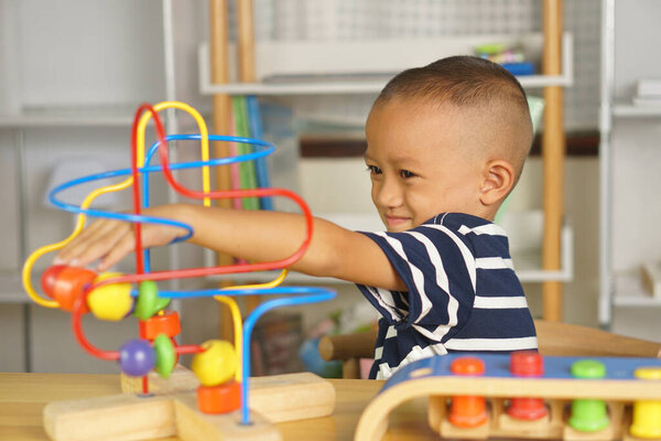 Мальчик играет с развивающими игрушками на столе в доме. Путем скольжения мяча по изогнутой стали