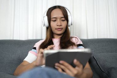 Asyalı kadın iş hakkında rahatlamak için iPad 'de müzik dinliyor.