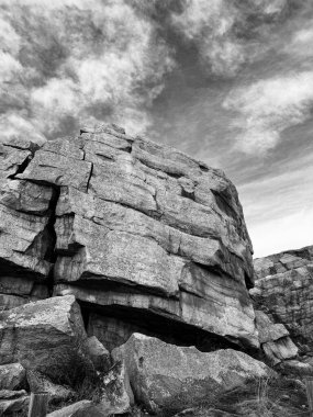 Karmaşık katmanları ve kalın dokuları olan yüksek bir kaya oluşumu siyah-beyaz bir kompozisyonda açıkça göze çarpar. Engebeli taşlar ve dramatik bulutlu gökyüzü arasındaki zıtlık derinlik katıyor ve sahneye zamansız, sinematik bir hava katıyor..