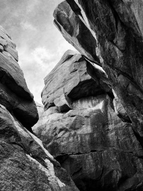 Devasa kaya oluşumlarının siyah-beyaz tasviri, onların kaba dokuları ışık ve gölge oyunlarıyla vurgulandı. Yukarı doğru açı, bulutlu bir gökyüzüne karşı kurulmuş kayaların heybetli boyutunu vurgular..