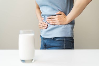 Laktoz intolerans konsepti. Kadın elinde bir bardak süt tutuyor ve midesi ağrıyor..