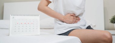 Monthly menstruation symptom period concept. Close up calendar marking on menstruation period day and woman have stomach pain as background.