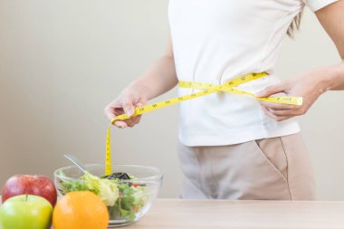Young slim woman measuring her waist by measure tape after a diet.