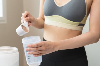 Young sporty woman pouring protein powder into a cup to make replacement food meal after workout