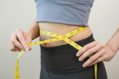 Young slim woman measuring her waist by measure tape after a diet