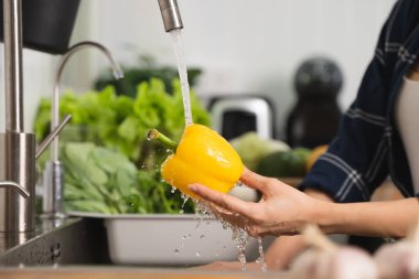 Close up of hands people washing vegetables by tap water at the sink in the kitchen to clean ingredient prepare a fresh salad.