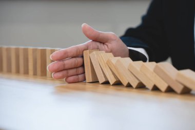 Protection finance from domino effect concept. Hands stop domino effect before destroy stack of money.