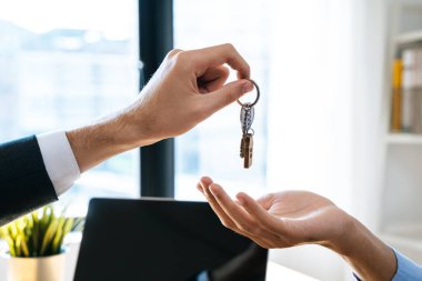 close up view hand of property realtor landlord giving key house to buyer tenant.