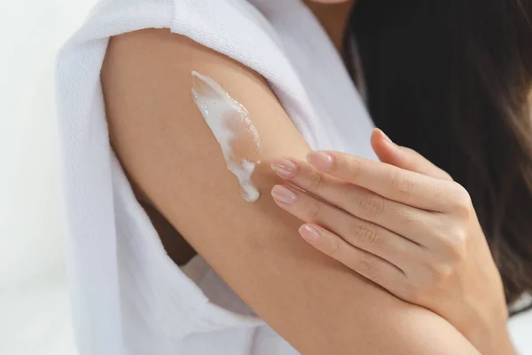 Young woman applying moisturizer cream to her arm in the morning routine.