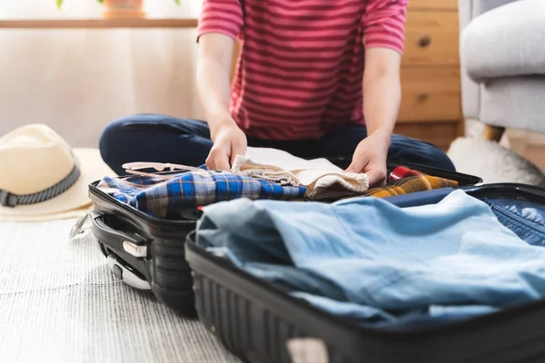 Preparing suitcase for summer vacation trip. Young woman checking accessories and stuff in luggage on the bed at home before travel.