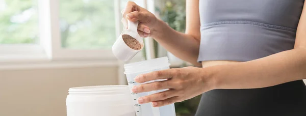 Young sporty woman pouring protein powder into a cup to make replacement food meal after workout