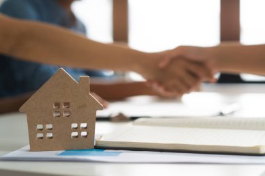 close up on model house on the table have client doing handshake business as background