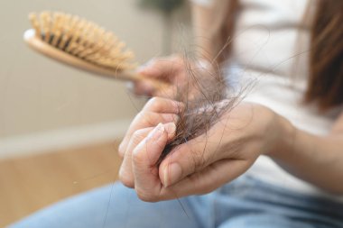 Hair fall problem concept. Shocked Asian woman looking at many hair lost in her hand and comb.