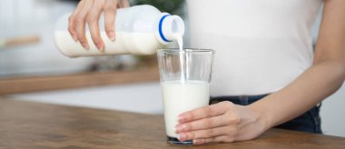 Close up hands woman pour pasteurized. milk to glass.