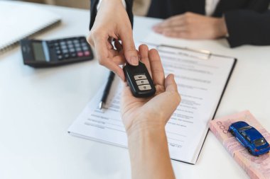 Concept car rental service. Close up view hands of agent giving car key to client that rent a vehicle in rental office.