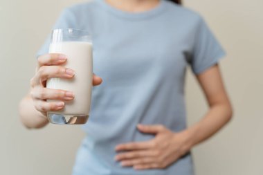 Laktoz intolerans konsepti. Kadın elinde bir bardak süt tutuyor ve midesi ağrıyor..