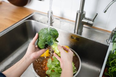 Close up of hands people washing vegetables by tap water at the sink in the kitchen to clean ingredient prepare a fresh salad.
