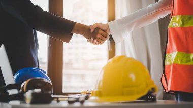 Successful deal, male architect shaking hands with client in construction site after confirm blueprint for renovate building.