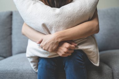 Unhappy anxiety young Asian woman covering her face with pillow on the cough in the living room at home.
