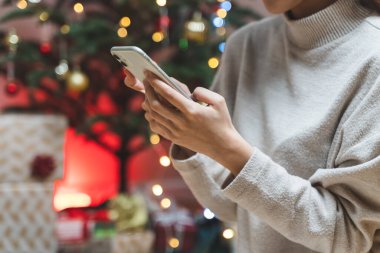 Close up hands of a woman using mobile phone and festive background