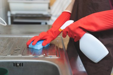 house maid cleaning sink in the kitchen with sponge and cleanser.