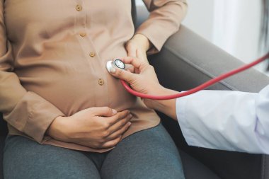 Doctor using stethoscope listening baby in pregnant belly at clinic / hospital