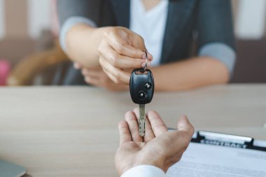 Car rental service concept. Close up view Hand of agent giving car key to customer after signed rental contract form.