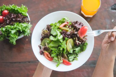 Eating healthy breakfast concept. Top view of woman holding dish of salad with variety vegetables and glass of orange juice on the floor in the morning at home.