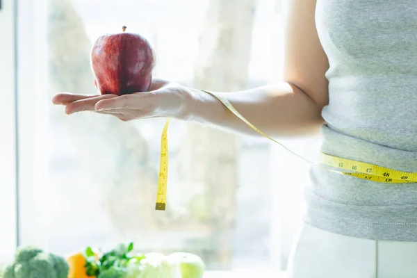 Healthy organic food for dieting woman concept. Woman carry red apple in front of healthy food and having a measure on her arm.
