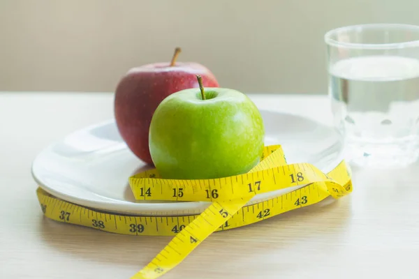 Good food for good health. Breakfast meal apple and water on the table and measure tape.