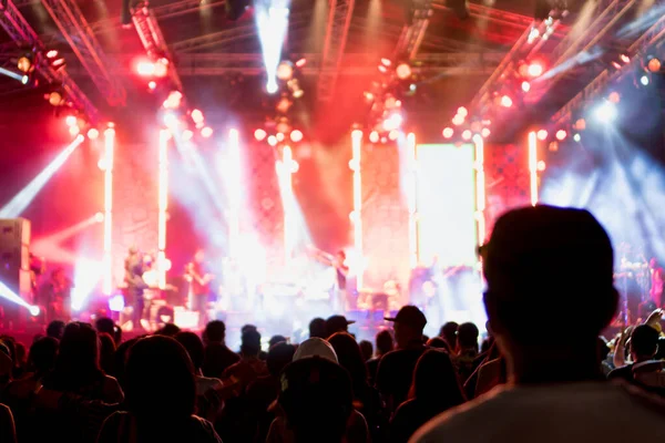 silhouettes of concert and people crowd in front of bright stage lights and blurry people on stage.