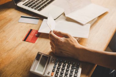 Close up hands of man holding credit card and calculating monthly invoices.
