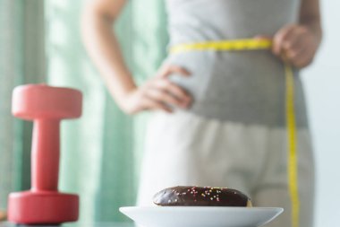 dietary for slim shape concept. Donut on the table have a woman measuring her waist as background.