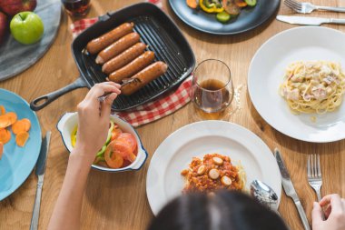 Aerial view of variety of food on the wooden table and friends eating dinner together.