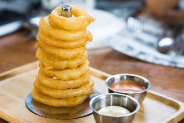 Delicious homemade appetizer. fried onion rings stack look like the tower serve with dip sauce on wooden tray.