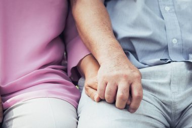 close-up view two seniors clasping hands together relaxed on sofa.