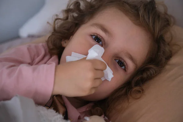 Sick girl wiping her nose with a tissue in her hand lying on the bed. seasonal virus, cold, catarrh