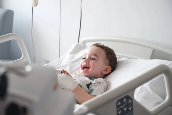 child in hospital lying in bed with mobile phone smiling