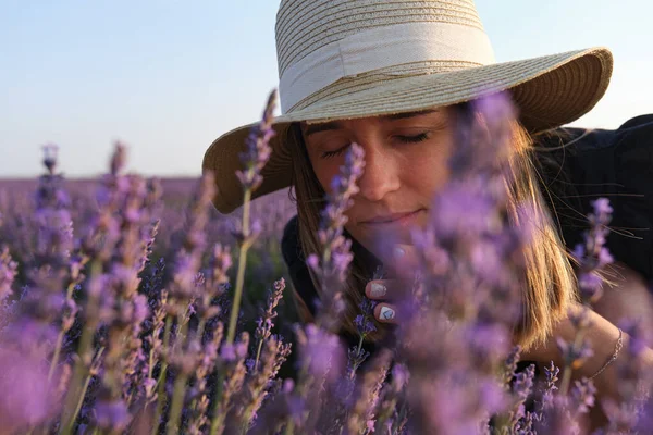 Relaxed woman enjoying the smell of lavender flowers in a field at sunset.