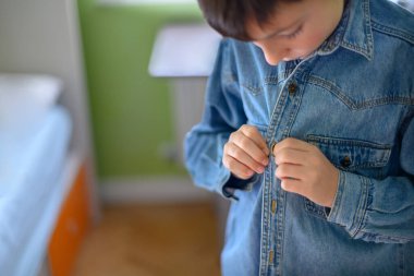 Boy fastens the button of a denim shirt