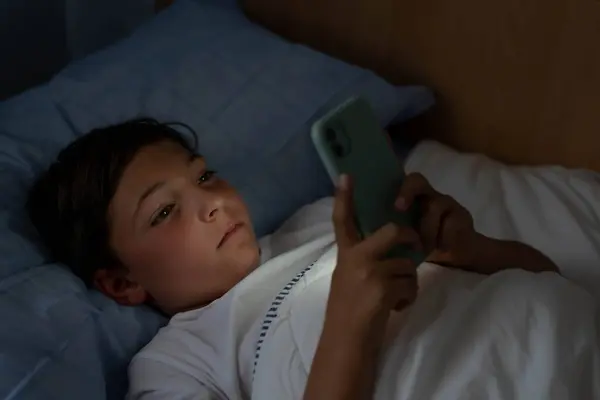 Boy sees cell phone lying in bed at night
