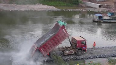 Taş, kaya ve çakıl yüklü bir kamyon, Mekong 'un bir kolu olan Nam Khan Nehri' ne, Luang Prabang, Laos, Asya 'ya arazi geliştirmek için yükünü boşaltıyor.