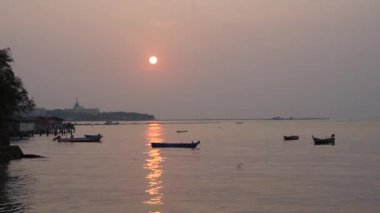 Deniz kenarında etkileyici bir gün batımı ve arka planda hızlandırılmış bir şehir manzarası.