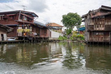 Chao Phraya nehrinin uzun kuyruklu ahşap botları ve Bangkok Tayland Asya 'daki konut binaları olan klong veya nehir kanalı.